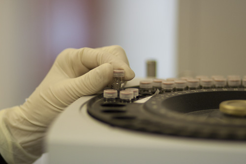 A hand with a latex glove places chemicals in a tube