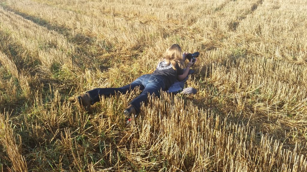 Woman lays in field with camera.
