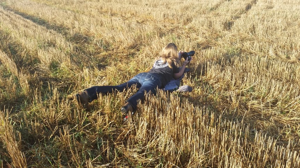 Woman lays in field with camera.