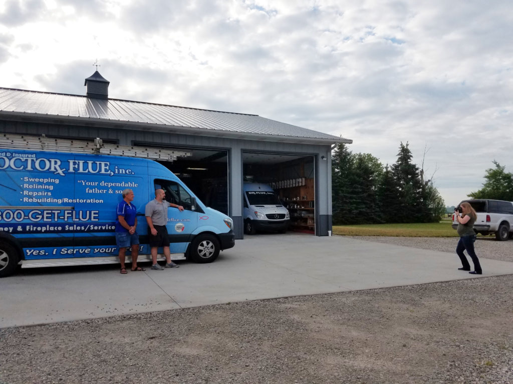 Woman photographs business owner in front of a work van.