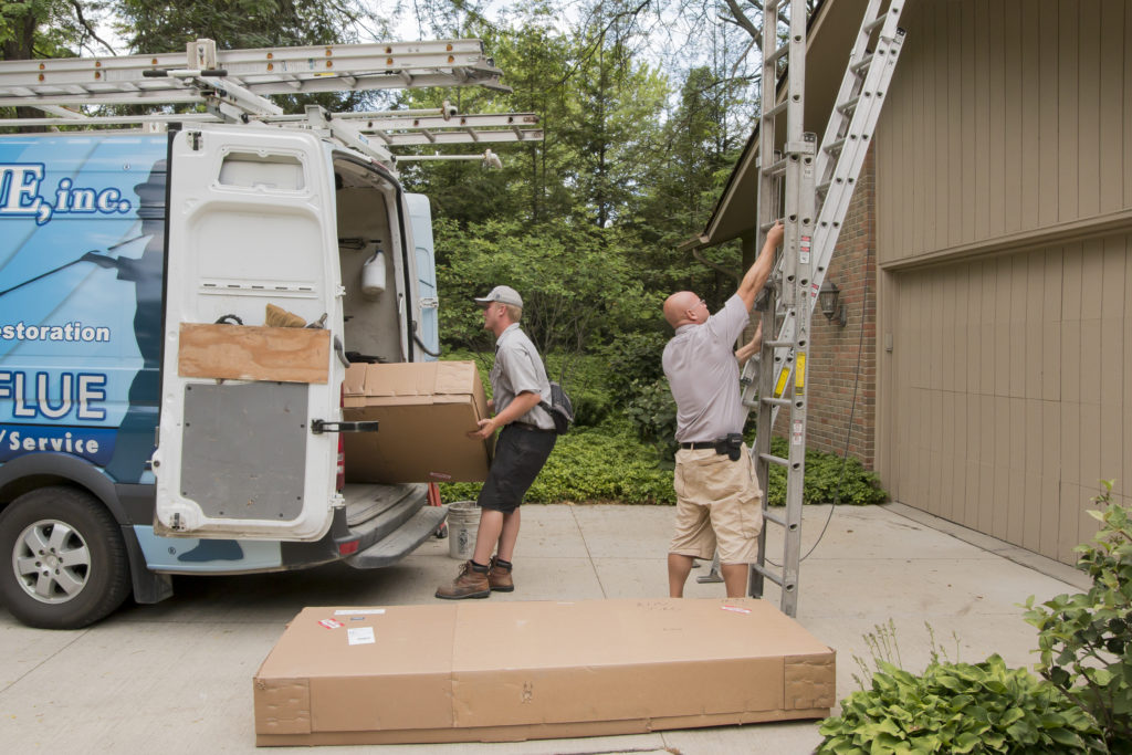Techs work to load a ladder into a work van.