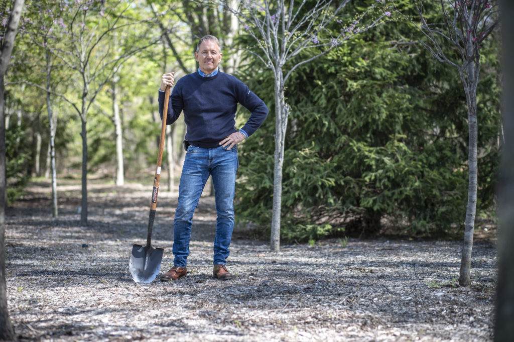 Ken stands with hand on hip, shovel in hand.